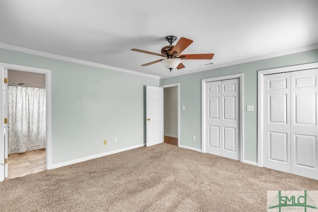 unfurnished bedroom featuring carpet, visible vents, baseboards, multiple closets, and crown molding