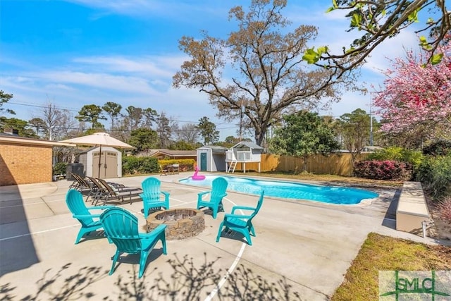 view of swimming pool featuring a fire pit, fence, a patio area, an outbuilding, and a storage unit