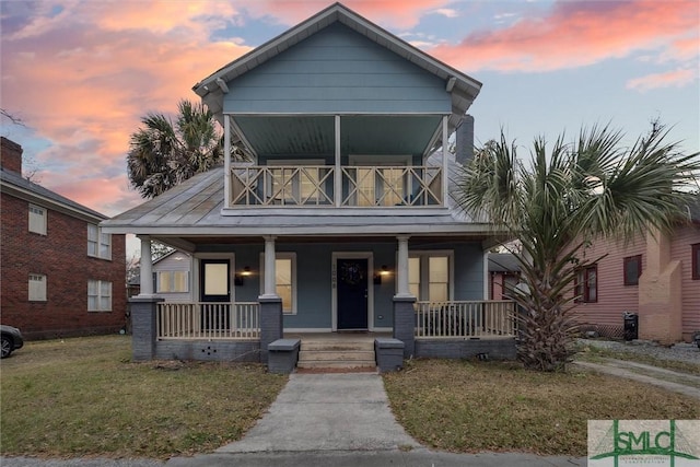 view of front of home with a porch, a balcony, and a lawn