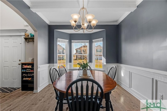 dining space with wainscoting, ornamental molding, an inviting chandelier, and wood finished floors