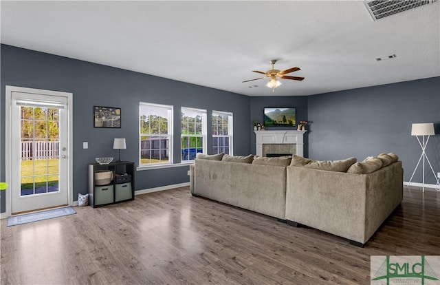 living area featuring ceiling fan, visible vents, wood finished floors, and a tiled fireplace