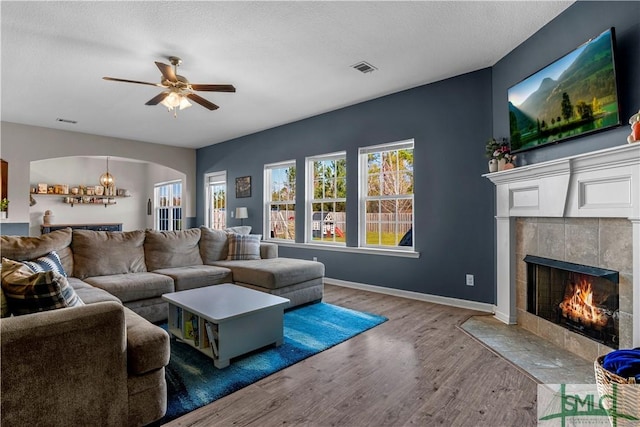 living room with wood finished floors, baseboards, a fireplace, arched walkways, and ceiling fan with notable chandelier