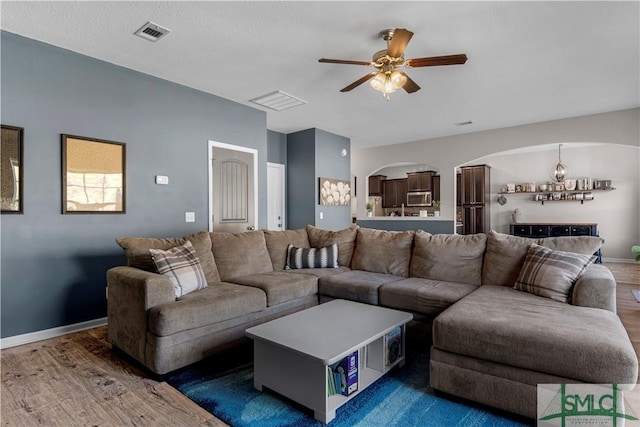 living room with visible vents, baseboards, wood finished floors, arched walkways, and a ceiling fan