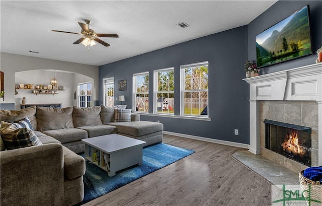 living room with visible vents, baseboards, a tile fireplace, wood finished floors, and arched walkways