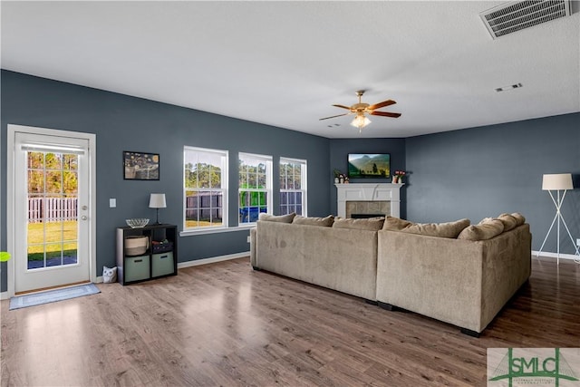 living area with ceiling fan, visible vents, wood finished floors, and a tile fireplace