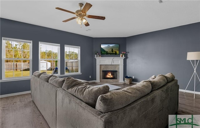 living room featuring a tiled fireplace, ceiling fan, baseboards, and wood finished floors