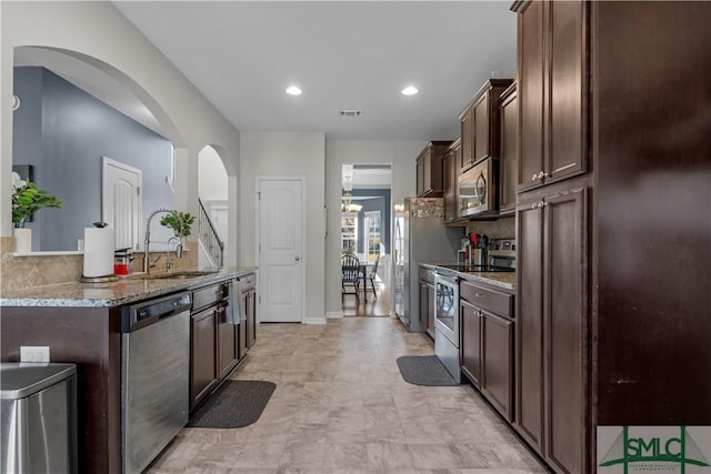 kitchen with dark brown cabinetry, appliances with stainless steel finishes, light stone countertops, and a sink