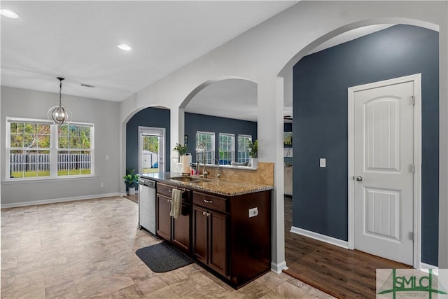 kitchen with light stone counters, a sink, dark brown cabinetry, pendant lighting, and stainless steel dishwasher