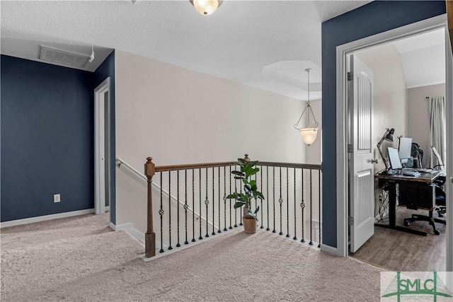 hall with carpet flooring, baseboards, visible vents, and an upstairs landing