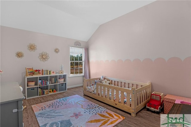 bedroom featuring baseboards, a crib, lofted ceiling, and wood finished floors