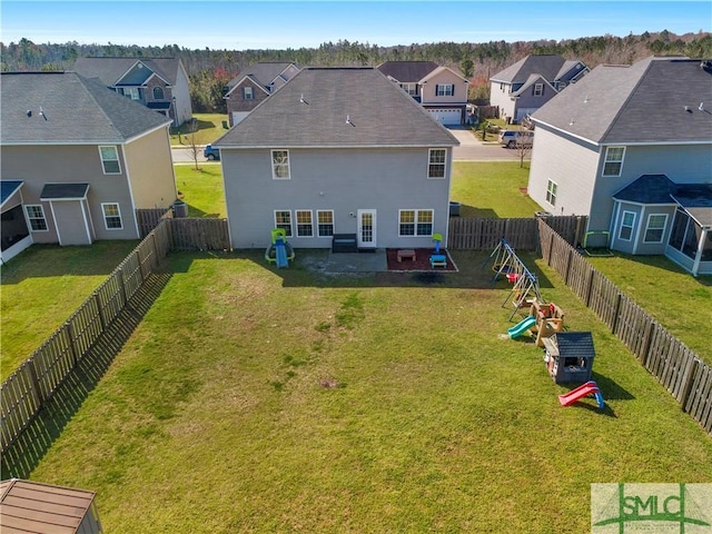 rear view of property featuring a residential view, a lawn, a fenced backyard, and a playground