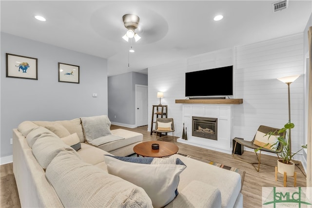 living area with a glass covered fireplace, baseboards, visible vents, and light wood-type flooring