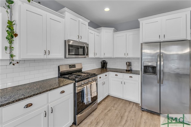 kitchen featuring dark stone countertops, backsplash, white cabinetry, stainless steel appliances, and light wood-style floors