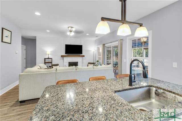 kitchen featuring wood finished floors, recessed lighting, a fireplace, stone countertops, and a sink