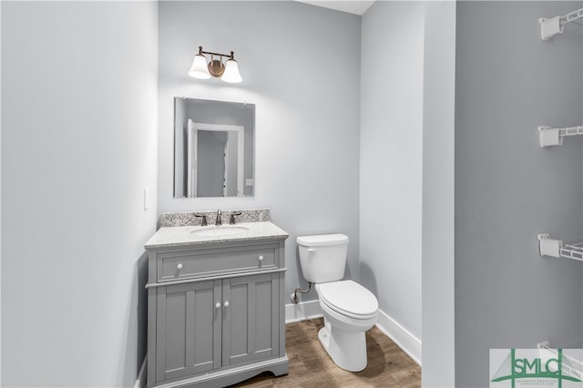 half bath with baseboards, toilet, wood finished floors, and vanity