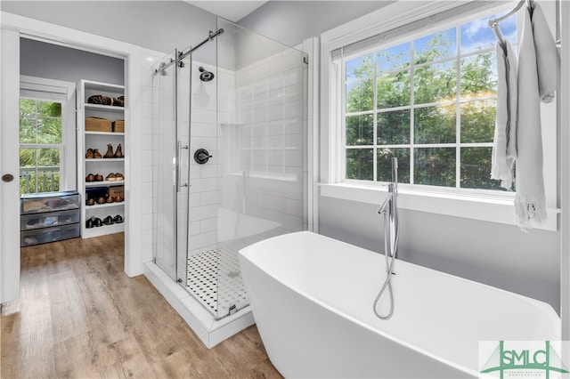 bathroom featuring a spacious closet, a freestanding tub, a stall shower, and wood finished floors