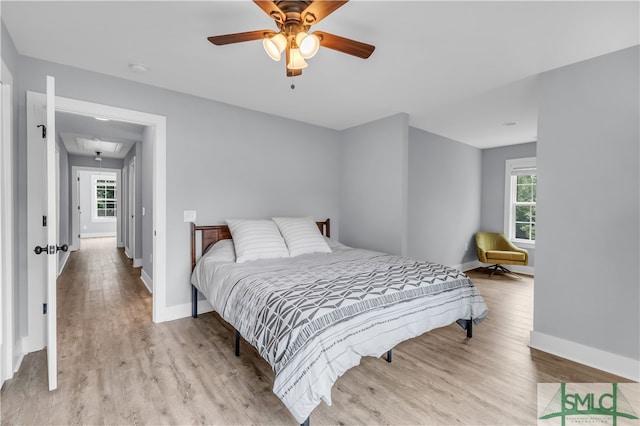 bedroom featuring a ceiling fan, attic access, baseboards, and light wood-type flooring