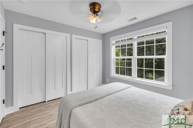 bedroom with visible vents, light wood-style flooring, two closets, and ceiling fan