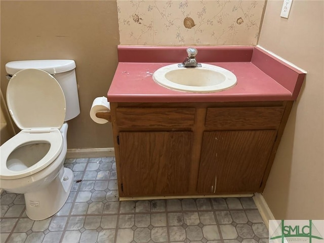 half bath featuring toilet, wallpapered walls, vanity, and baseboards