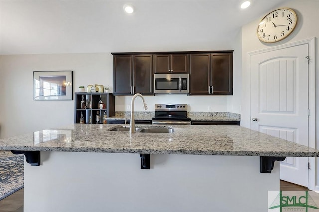 kitchen with a kitchen island with sink, a sink, stainless steel appliances, a breakfast bar area, and dark brown cabinets