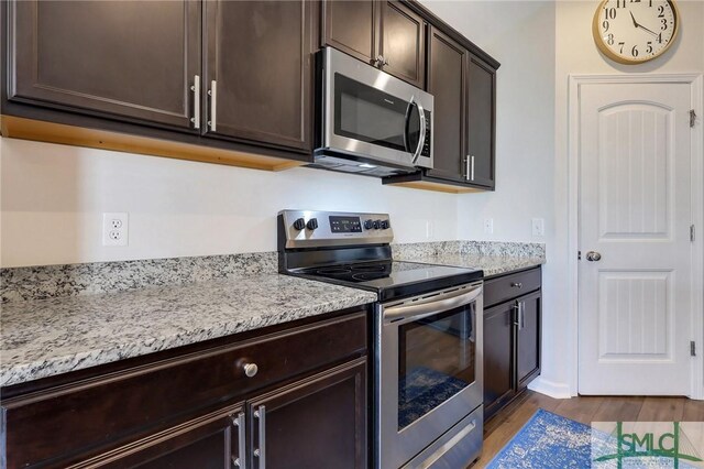 kitchen with dark brown cabinets, appliances with stainless steel finishes, light stone countertops, and wood finished floors