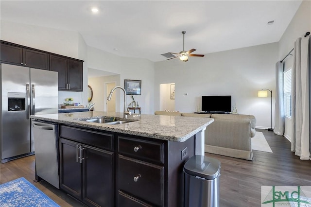 kitchen with dark wood finished floors, an island with sink, stainless steel appliances, a ceiling fan, and a sink