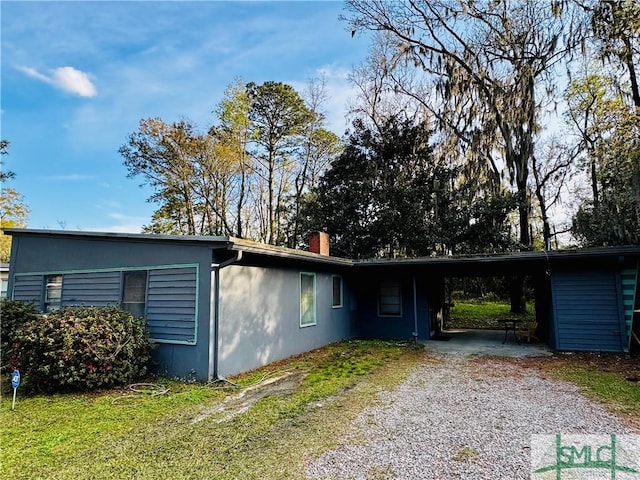 view of front of home with an attached carport, a chimney, gravel driveway, and stucco siding