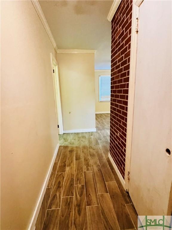 corridor featuring brick wall, wood finished floors, baseboards, and ornamental molding