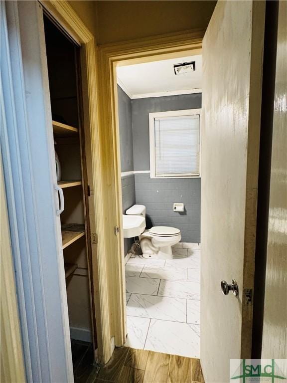 half bathroom featuring tile walls, toilet, marble finish floor, and ornamental molding