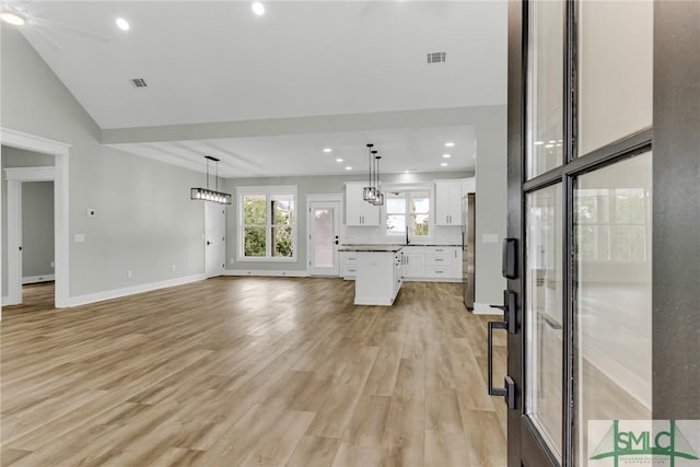 unfurnished living room featuring visible vents, light wood-style flooring, baseboards, and vaulted ceiling