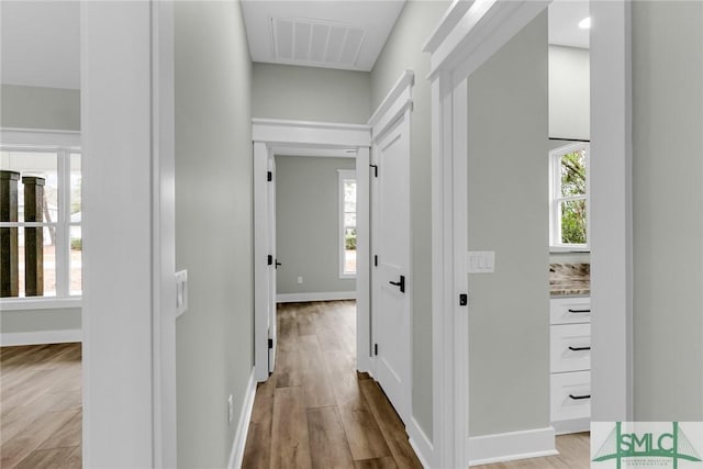 hall with visible vents, baseboards, and wood finished floors