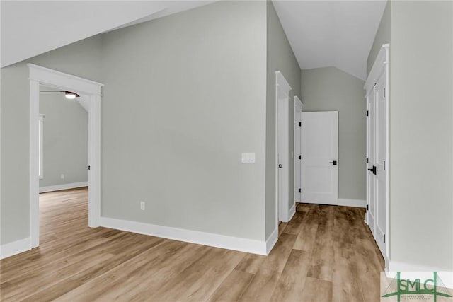 hallway featuring lofted ceiling, baseboards, and light wood finished floors