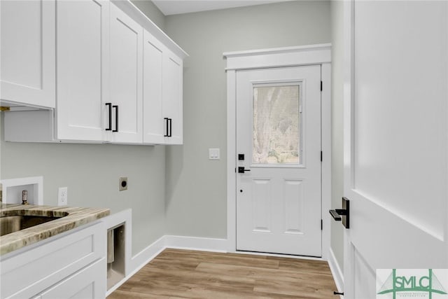 washroom featuring electric dryer hookup, light wood-style flooring, a sink, cabinet space, and baseboards