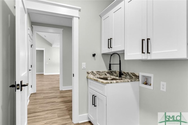 laundry room with hookup for a washing machine, baseboards, cabinet space, a sink, and light wood-style floors