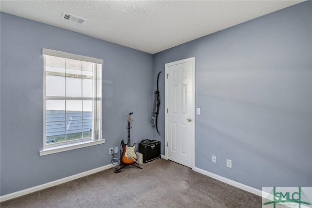 spare room with a textured ceiling, baseboards, visible vents, and carpet