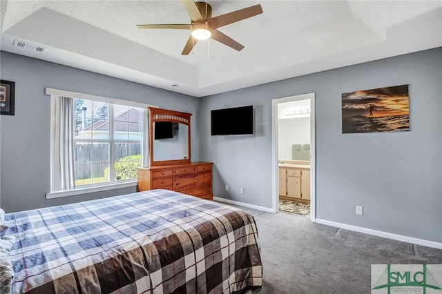 carpeted bedroom with ceiling fan, a raised ceiling, ensuite bath, baseboards, and visible vents