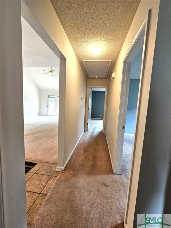 corridor with a textured ceiling, baseboards, attic access, and carpet