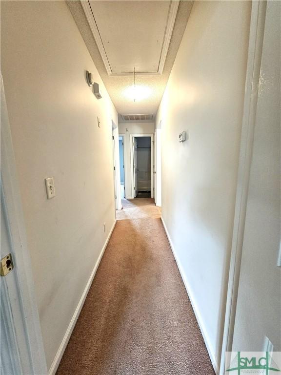 corridor with light colored carpet, attic access, baseboards, and visible vents
