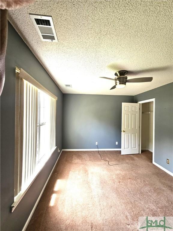 carpeted spare room with baseboards, a ceiling fan, visible vents, and a textured ceiling