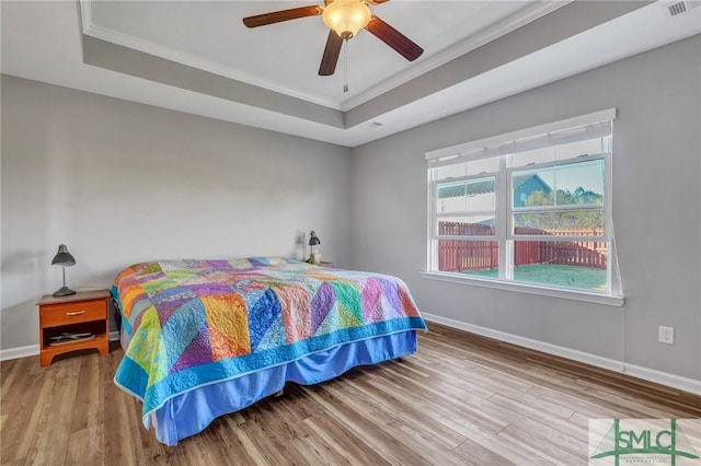 bedroom with a tray ceiling, wood finished floors, and baseboards