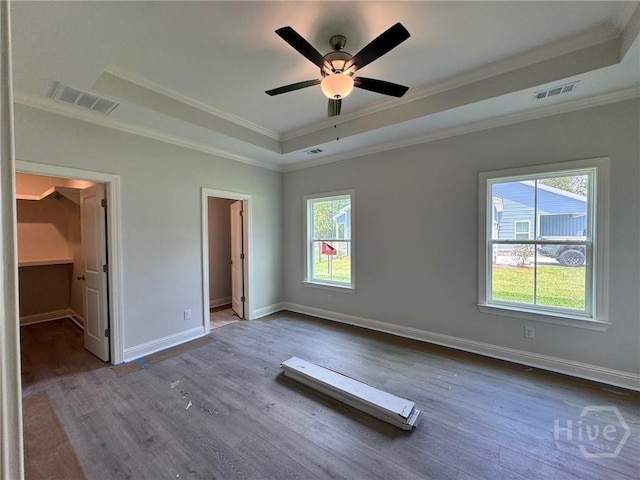 109 Ennis Rd, Pembroke, GA 31321 - unfurnished bedroom featuring a walk in closet, a tray ceiling, ornamental molding, multiple windows, and dark wood-style floors