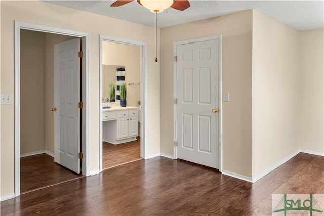 interior space featuring a textured ceiling, baseboards, dark wood-type flooring, and a ceiling fan