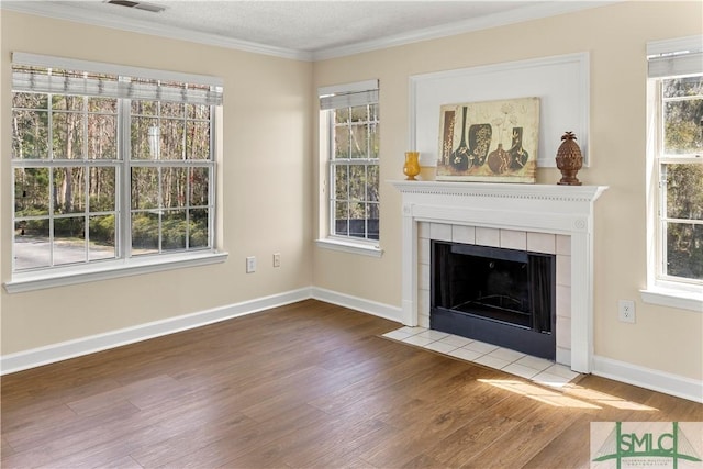 unfurnished living room with a tiled fireplace, crown molding, plenty of natural light, and wood finished floors