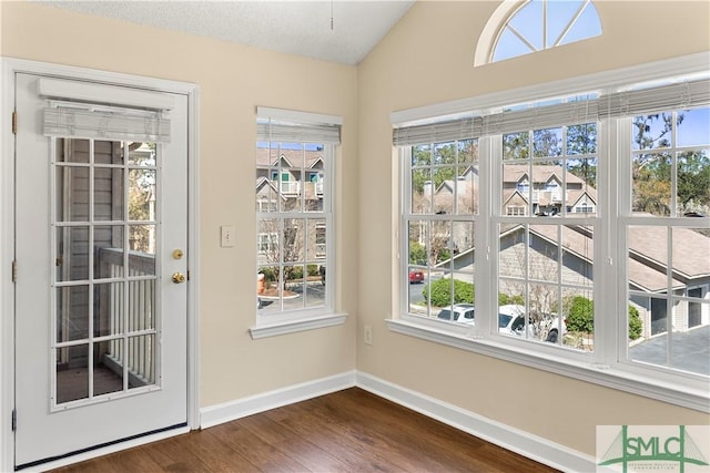 doorway to outside featuring vaulted ceiling, plenty of natural light, dark wood-style floors, and baseboards