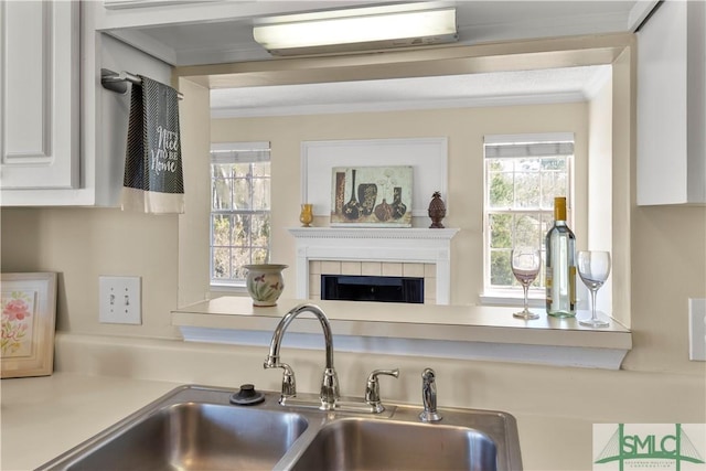 kitchen with a tiled fireplace, ornamental molding, white cabinetry, and a sink