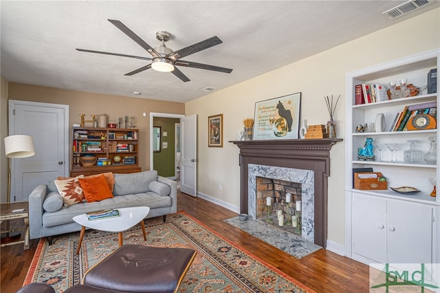 living area featuring visible vents, baseboards, a fireplace, wood finished floors, and a ceiling fan