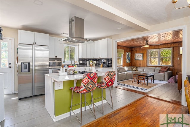 kitchen featuring open floor plan, light countertops, appliances with stainless steel finishes, island range hood, and white cabinets