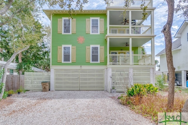 coastal home with a balcony, fence, driveway, an attached garage, and ceiling fan