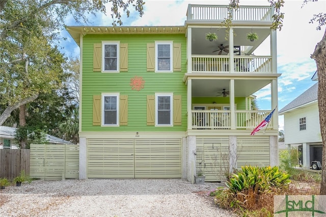 coastal home with a balcony, driveway, a ceiling fan, and fence