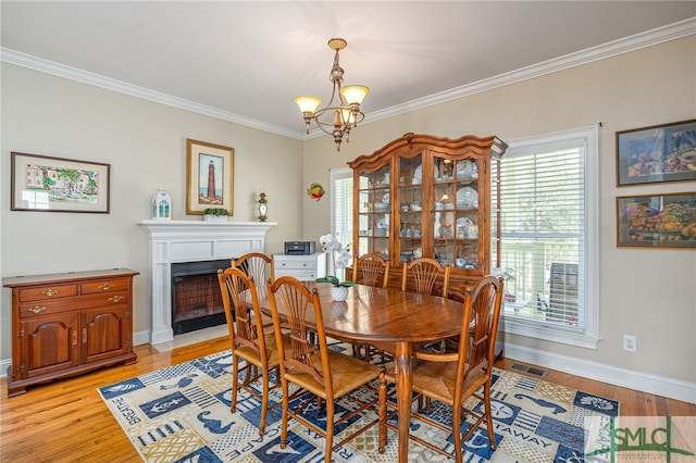 dining room with light wood-type flooring, a fireplace with flush hearth, a notable chandelier, visible vents, and crown molding